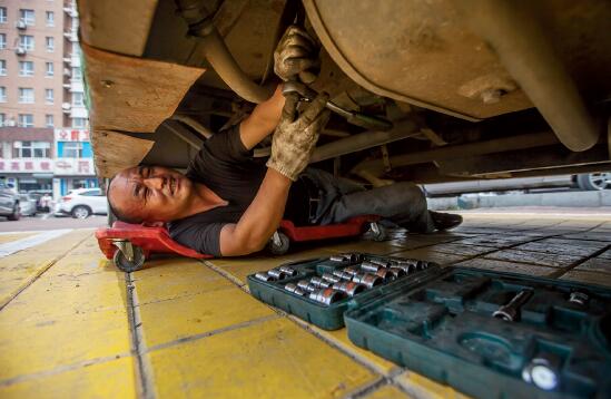 p43-1 8 月2 日，吉林省长春市，一名公交修理工正在对车辆发动机进行维修。他手上都是黑黑的油污，一旁车厢内的温度计显示一直停留在50℃最高值。CFP