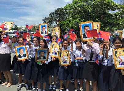 柬埔寨当地群众手持中柬两国领导人画像、挥舞两国国旗和花束，热烈欢迎习近平到访。人民日报全媒体平台记者杜尚泽 摄