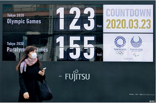 p103 3 月23 日，一名行人戴着口罩在日本东京新桥地区经过显示东京奥运会和残奥会倒计时的大屏幕。