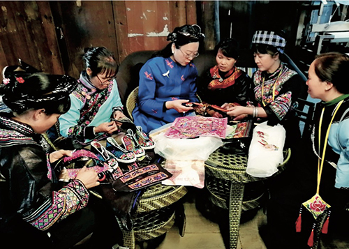 53 2018 年11 月，依文集团董事长夏华（左三）在贵州省黔西南州的村寨里与布依族绣娘讨论纹样的